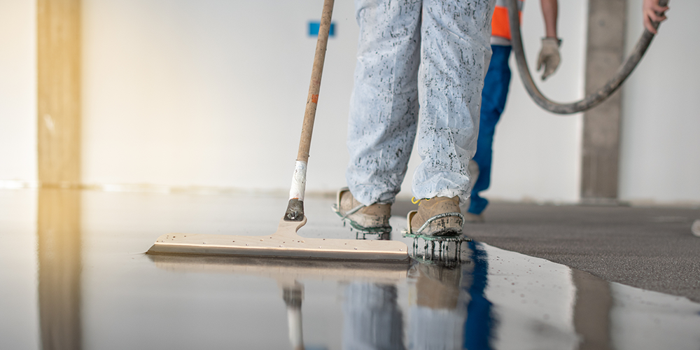 Worker spreads epoxy coating on concrete floor.
